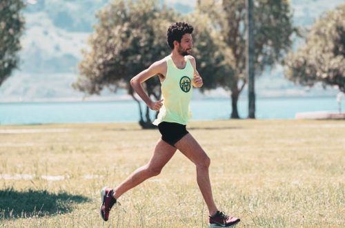 Side view of young determined male athlete in sportswear running on lawn in park near lake in sunny morning