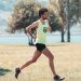 Side view of young determined male athlete in sportswear running on lawn in park near lake in sunny morning