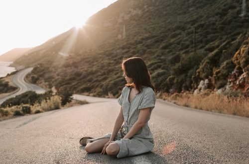 A woman sitting on a coastal road in Antalya during sunset, offering a serene landscape view.